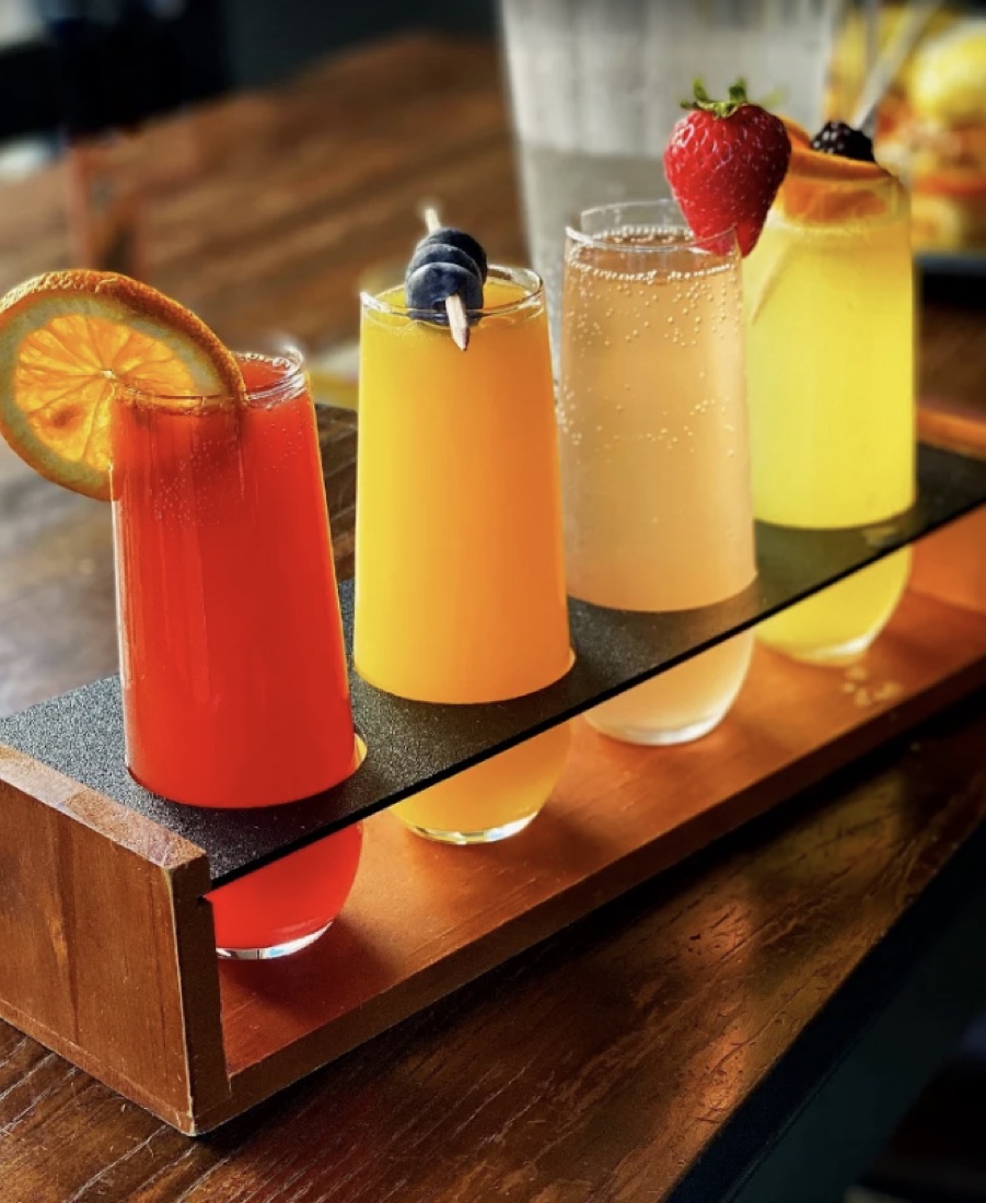 Flight of colorful mimosas on a wooden board at Honey & Herb brunch